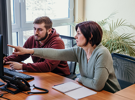 Two pro et con employees in front of a desktop pc